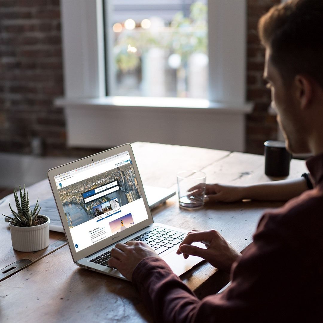 A Man is Sitting at a Table Using a Laptop Computer — Construction Services in Southport, QLD