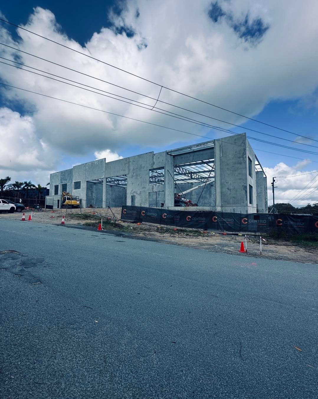 Construction site with a concrete building frame and blue sky. Road and safety cones in foreground.