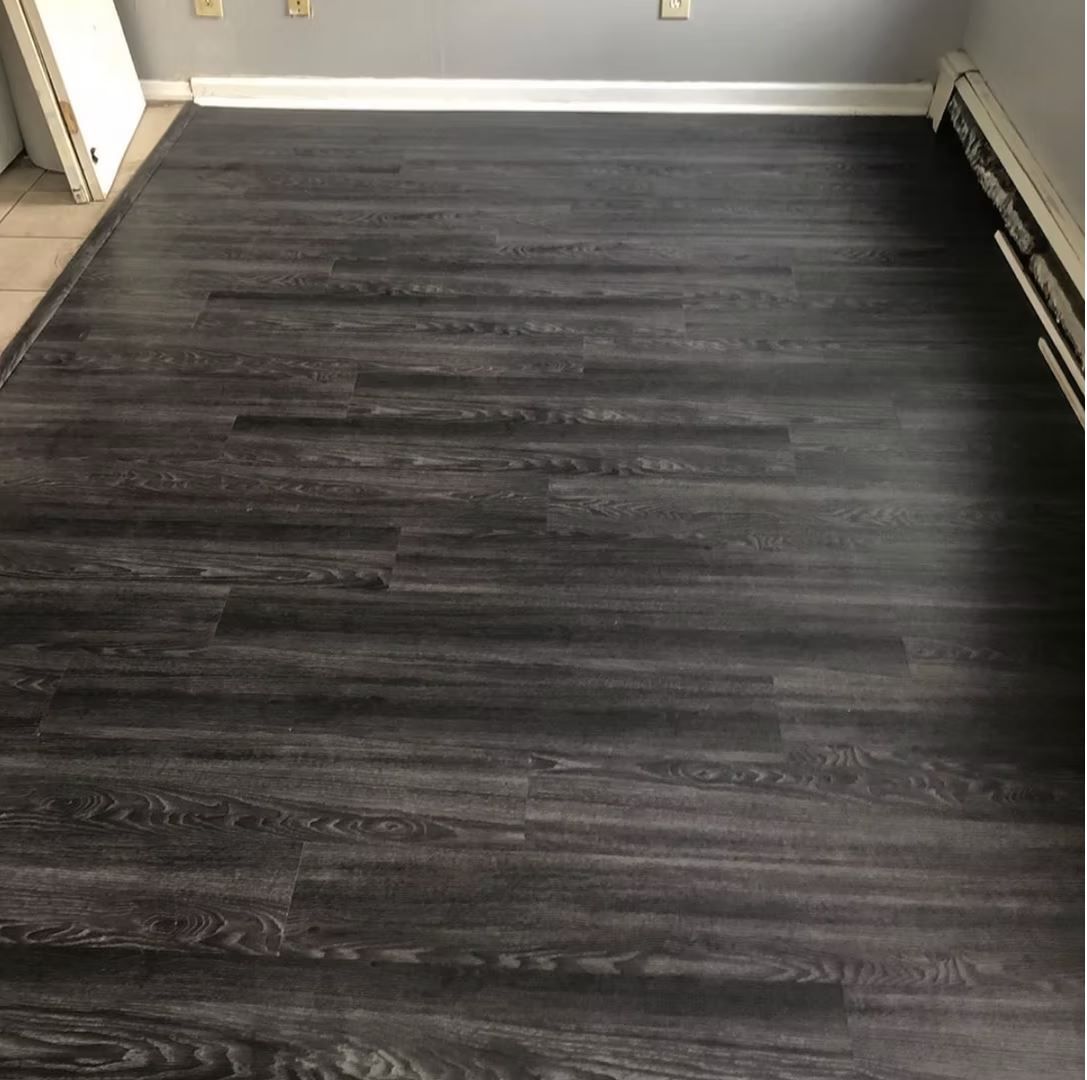 Dark gray wood-look flooring in a room with white baseboards and a radiator.