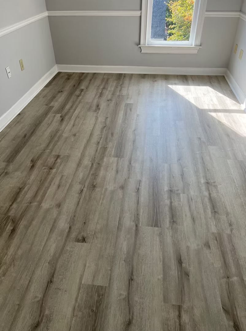 Gray wood-look flooring in an empty room, sunlight coming through the window.