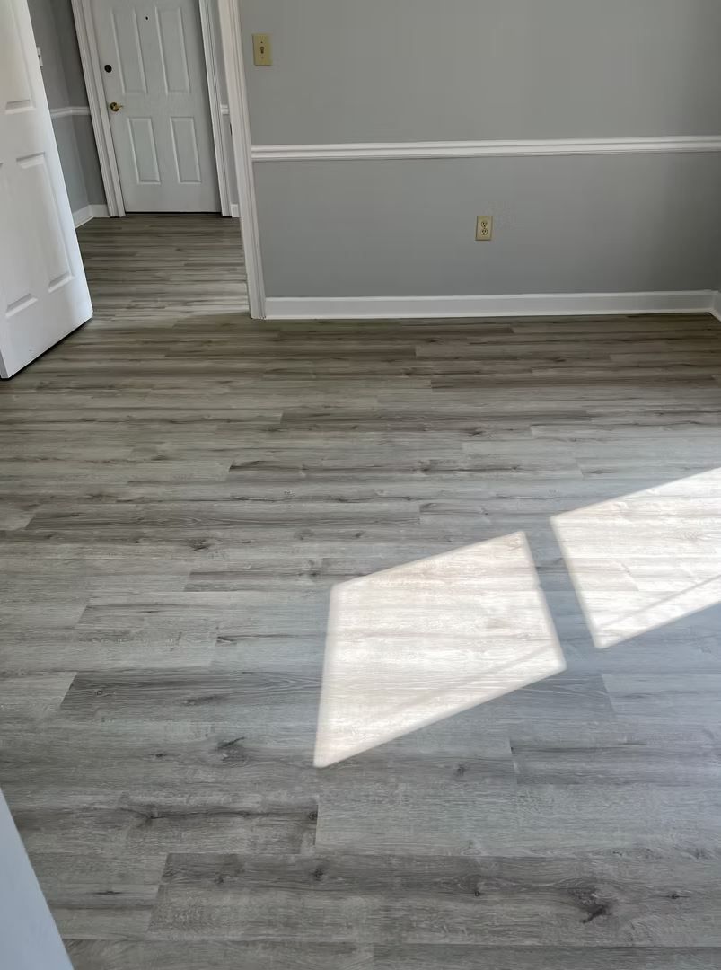 Gray wood-look flooring in a room with white trim, and a doorway leading to a white door.