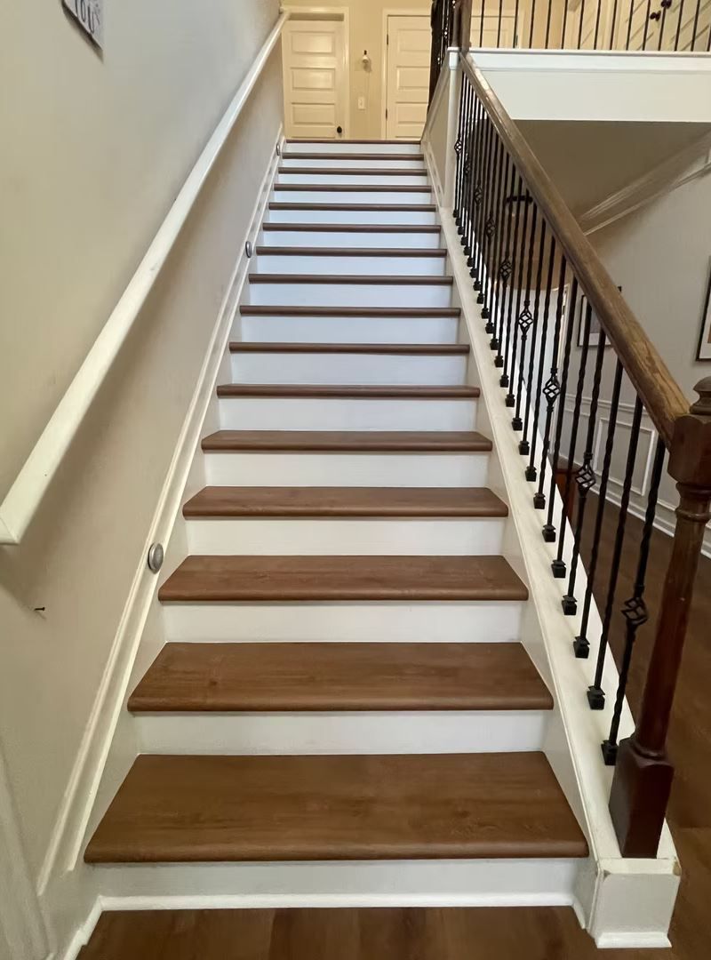 Staircase with wooden steps and white risers, with a white handrail and dark metal railing on the side.