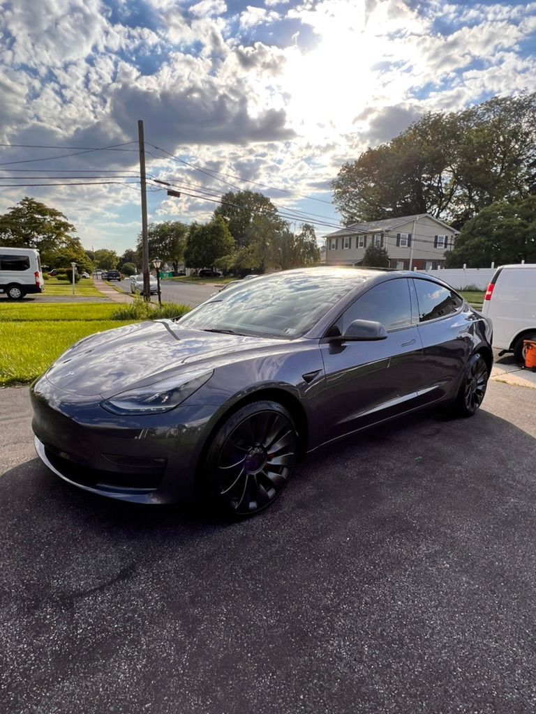 A tesla model 3 is parked in a driveway.
