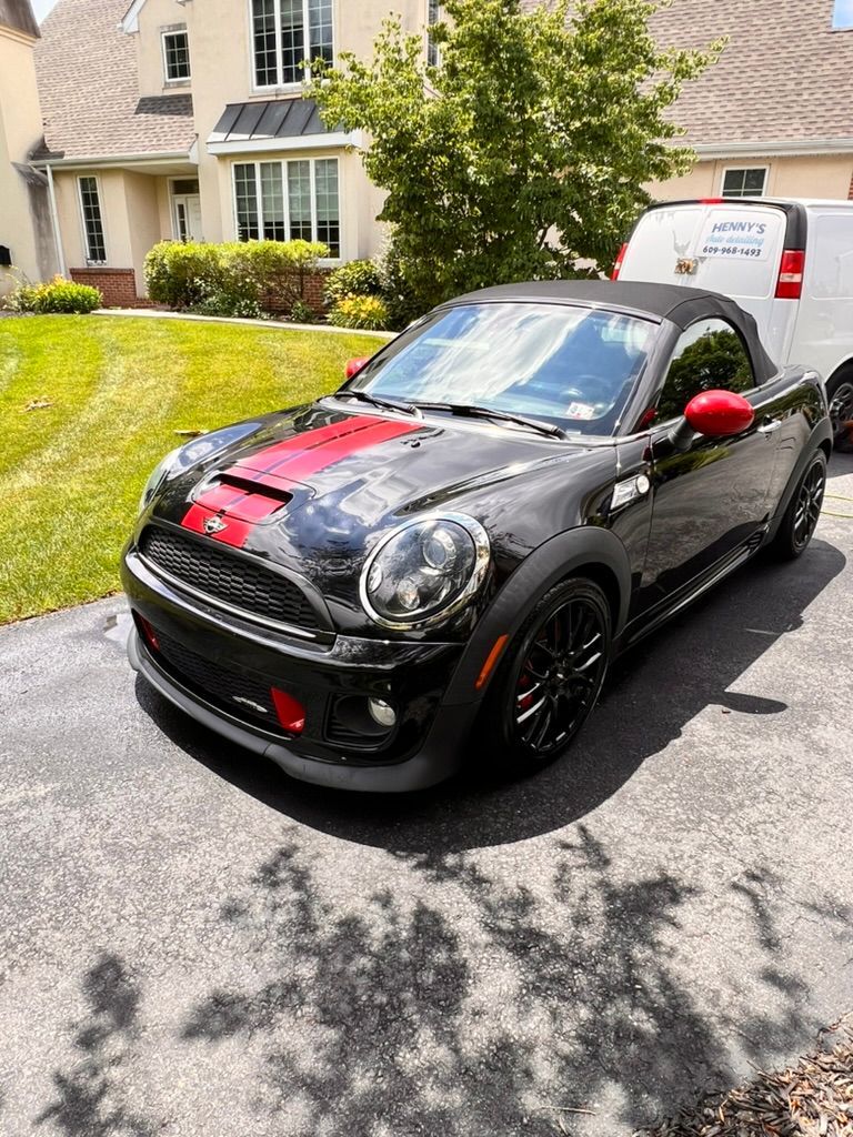 A black mini cooper convertible is parked in a driveway in front of a house.