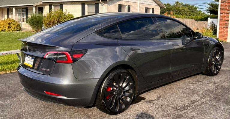 A tesla model 3 is parked in a driveway in front of a house.