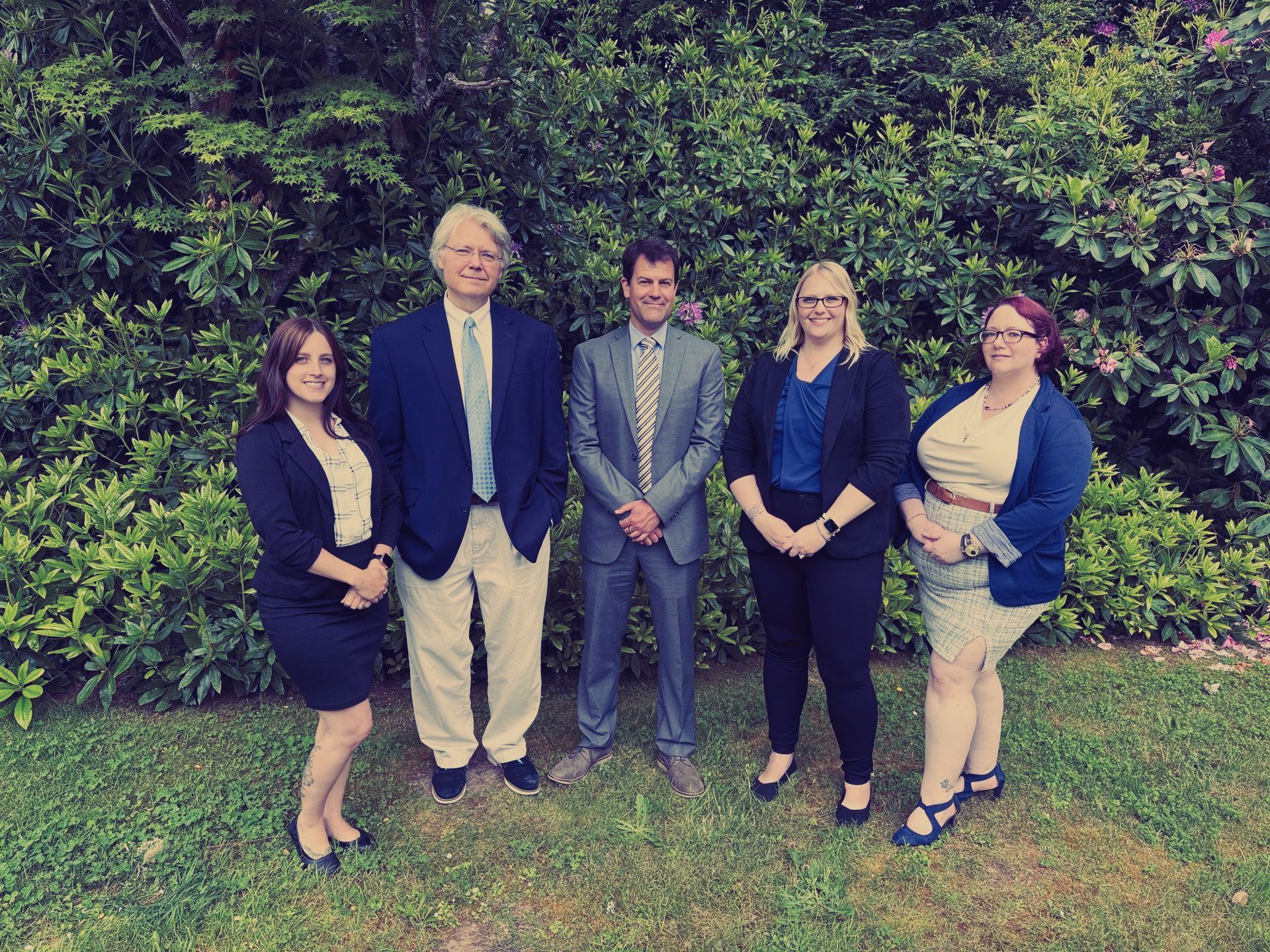 A group of people are posing for a picture in front of a bush.