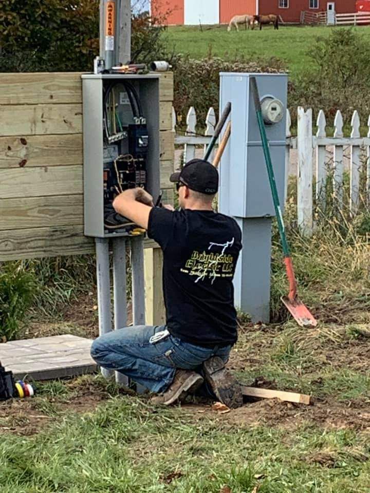 A man is kneeling down in the grass working on an electrical box.