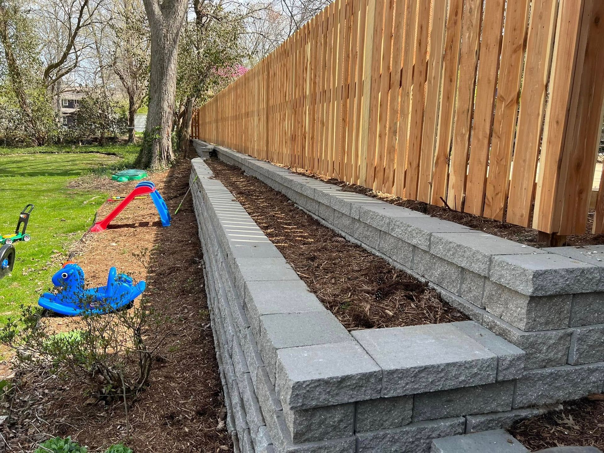 A wooden fence surrounds a brick wall in a backyard.