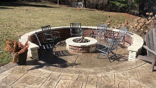 There is a fire pit in the middle of the patio with chairs around it.
