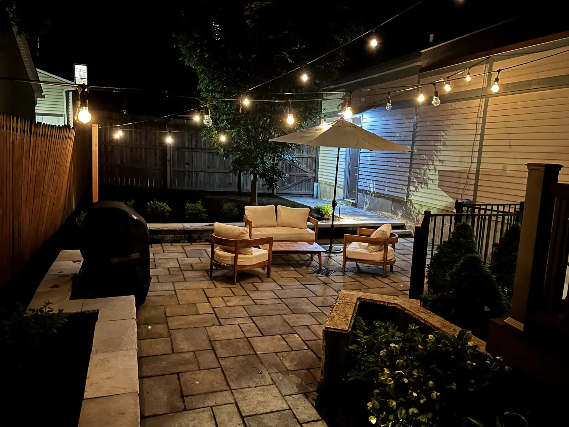 A patio with a couch , chairs , and umbrella at night.
