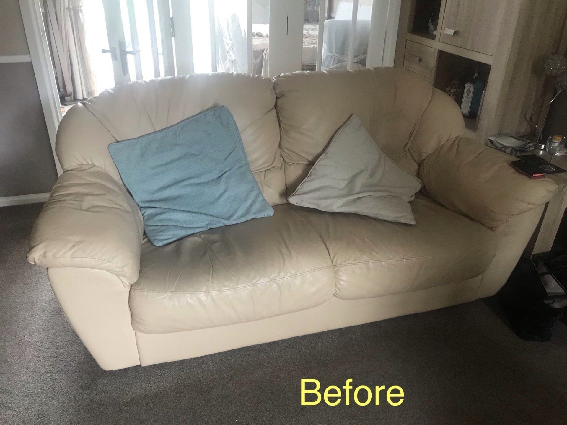 Old looking cream leather sofa with worn out blue cushions