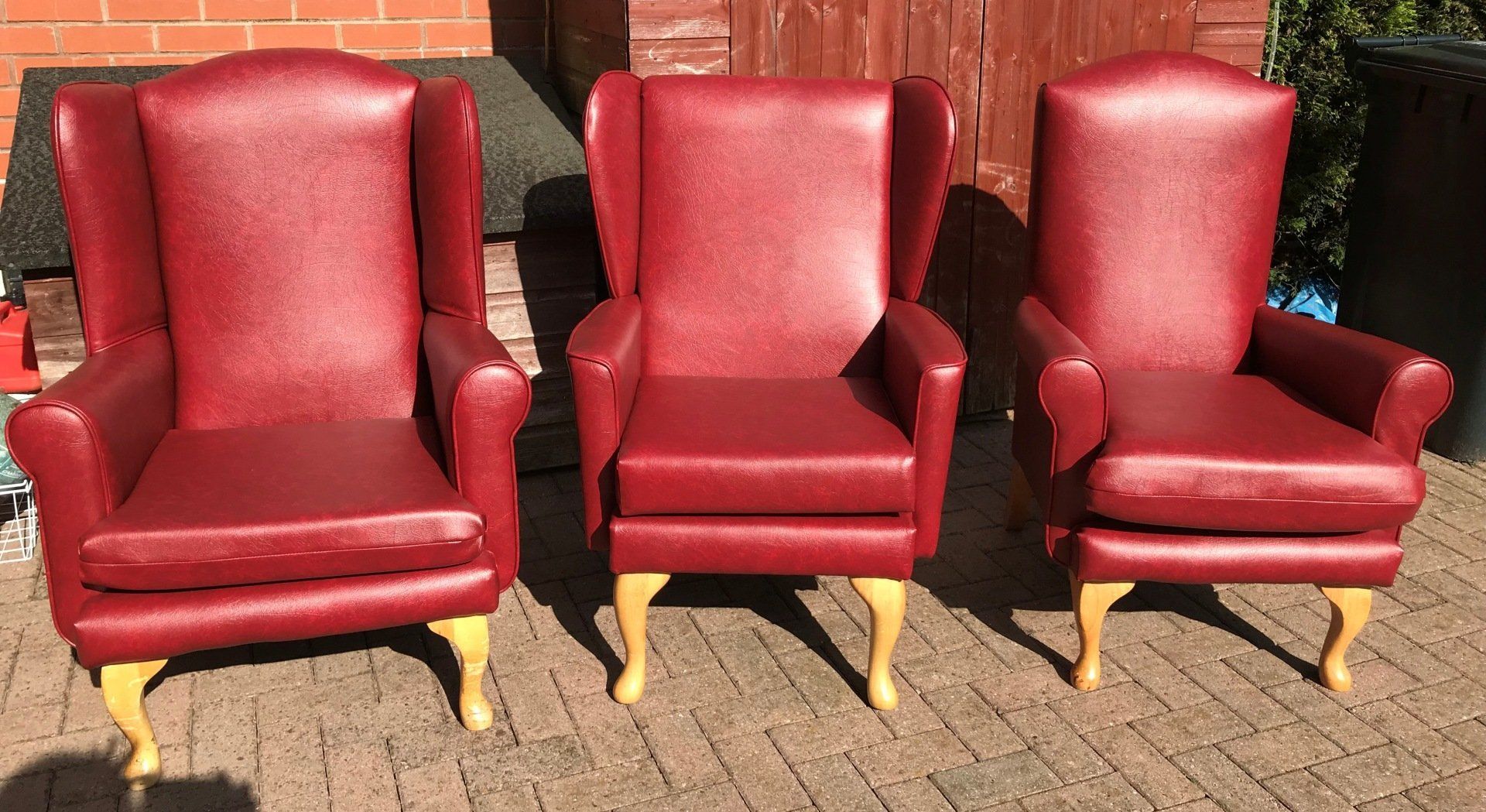 Three red leather armchairs outside in sunlight