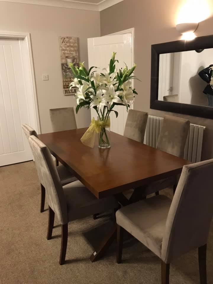 Dining table with chairs around it, lilies in a vase and a mirror on the wall