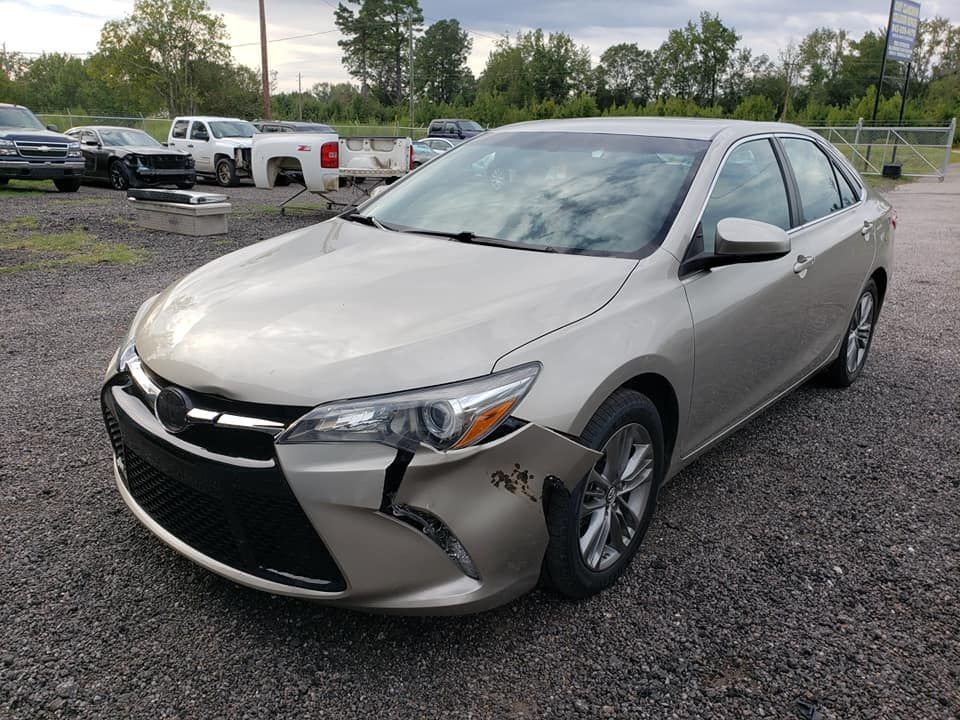 a toyota camry with a damaged front bumper is parked in a gravel lot .