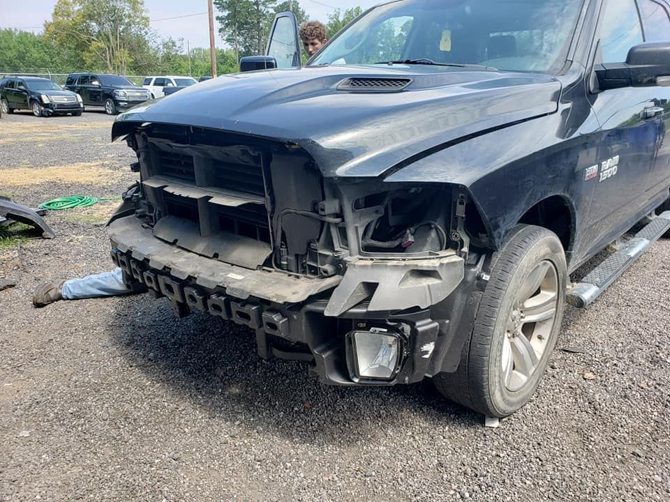 a black ram truck with a damaged front end is parked in a gravel lot .