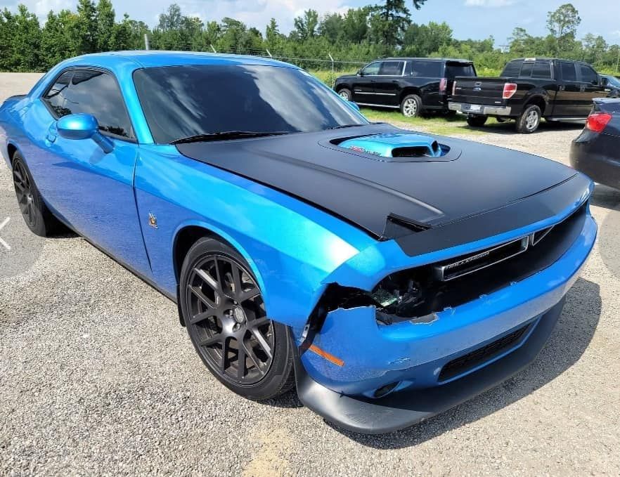 a blue dodge challenger with a black hood is parked in a parking lot .