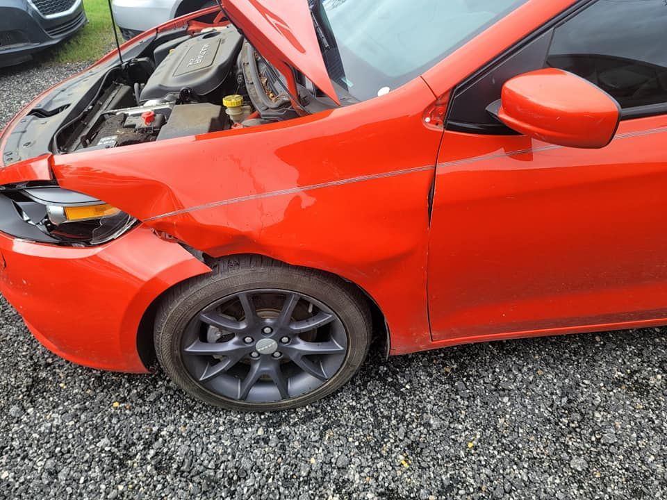 a red car with the hood up is parked on gravel .