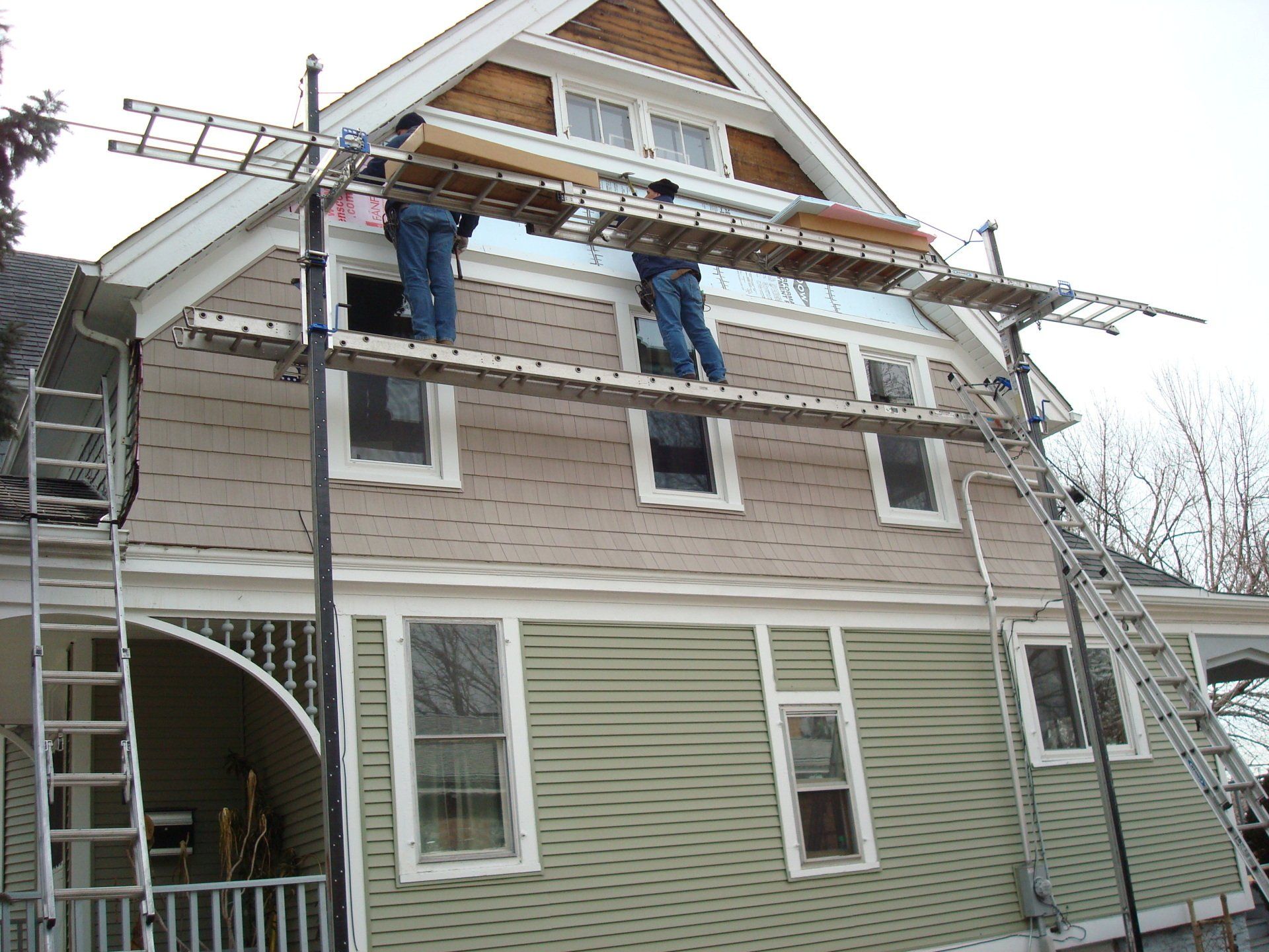 Two men are standing on scaffolding on the side of a house