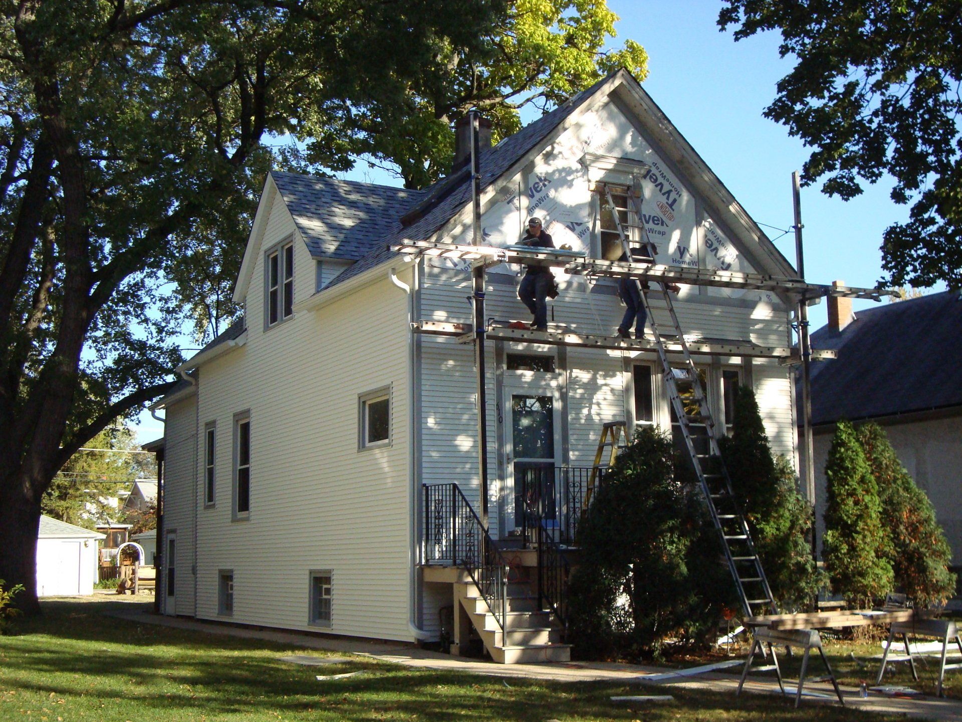 Two men are painting the side of a white house