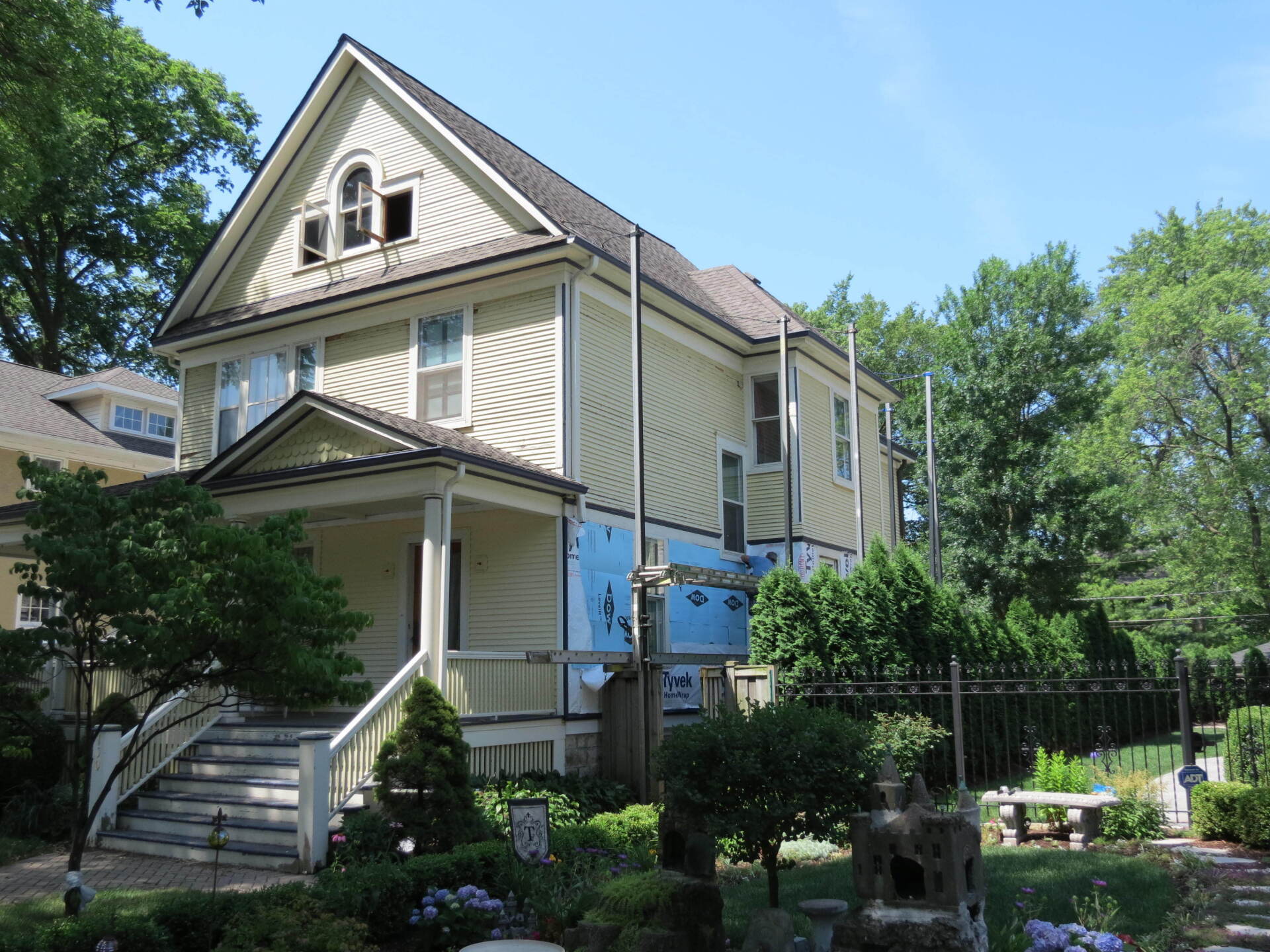 A large house with a porch and stairs is surrounded by trees and bushes.
