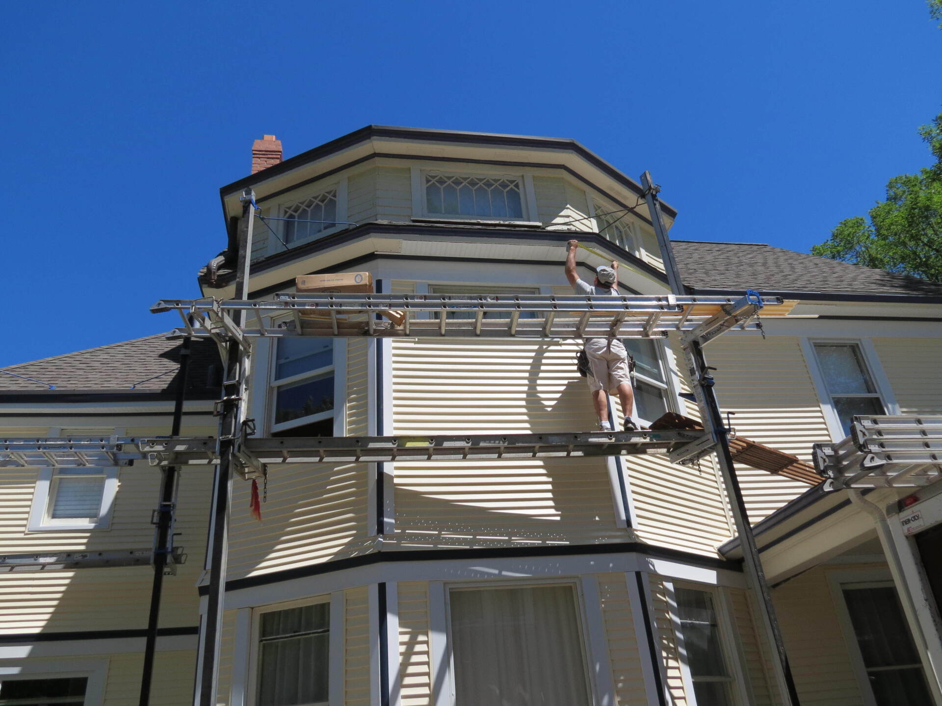 A man is painting the side of a house with a ladder.
