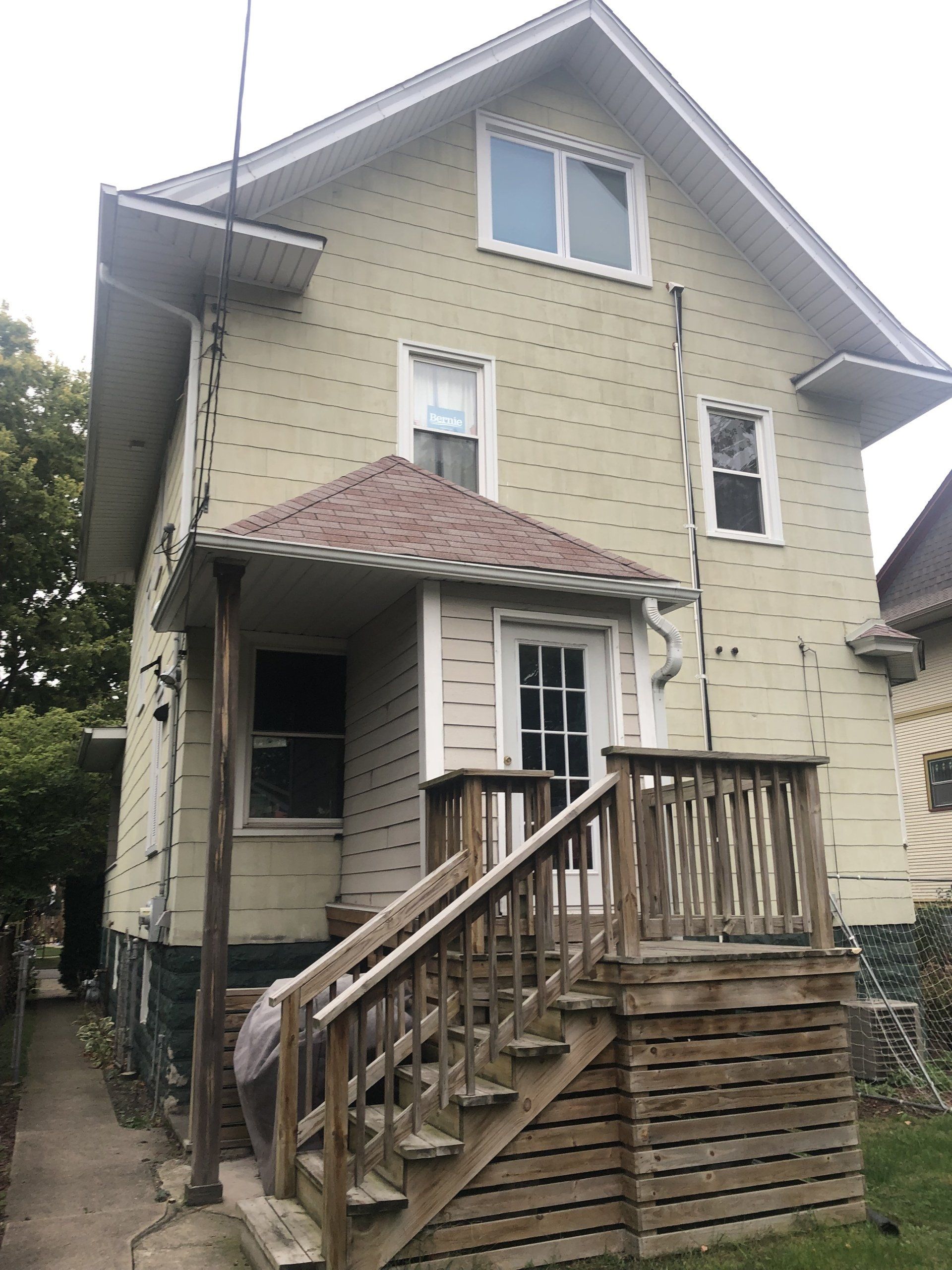 A yellow house with a wooden deck and stairs