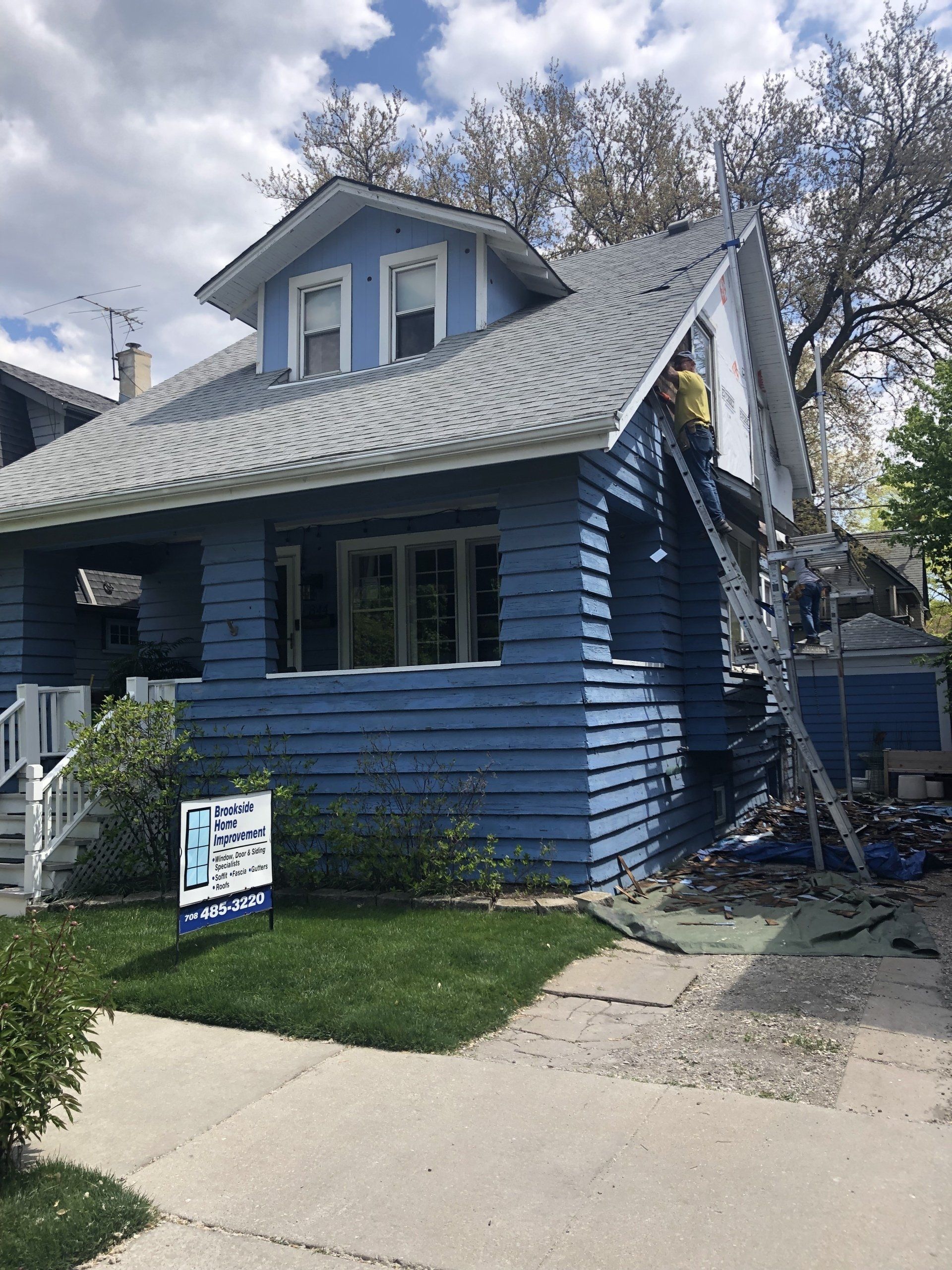 A blue house is being painted by a man on a ladder.
