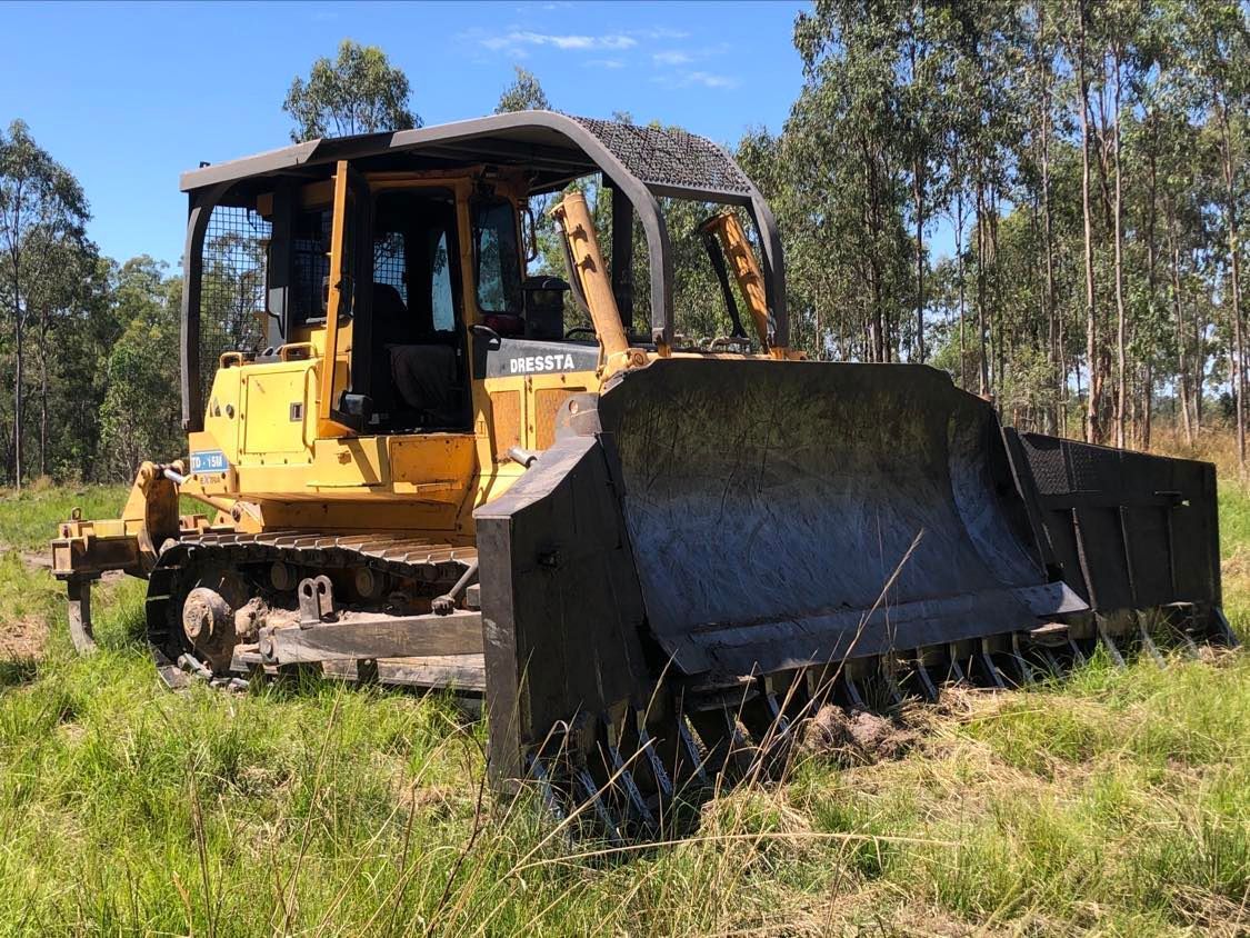 Yellow bulldozer clearing a grassy field near a stand of trees.