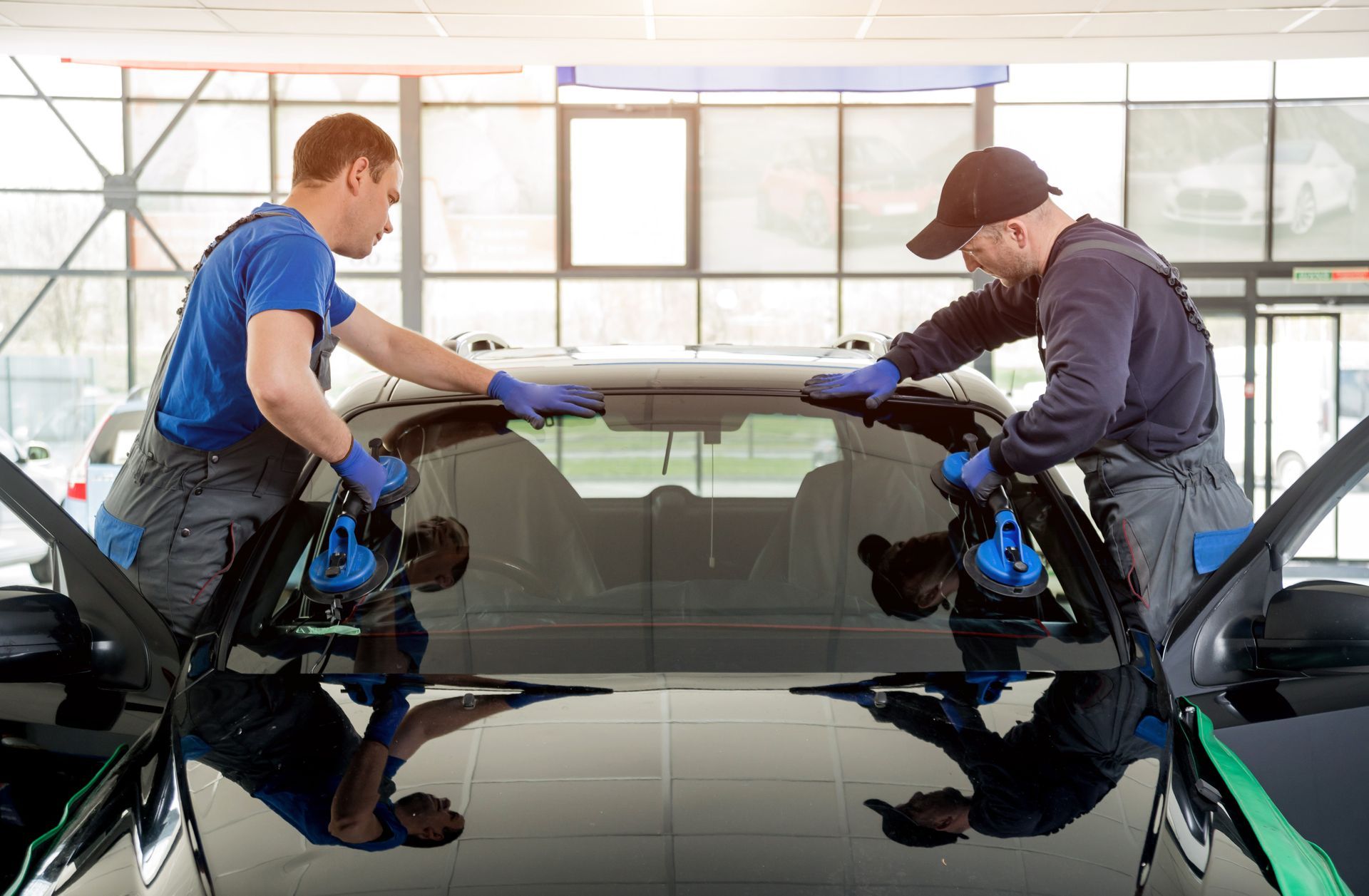 Two workers installing a windshield on a black car in a shop.