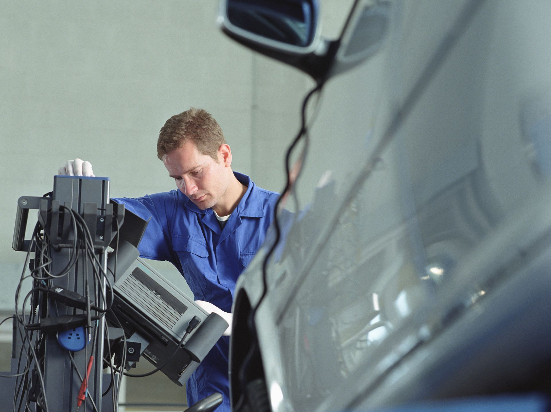 Mechanic in blue overalls working on a car, checking alignment with a machine in a garage.