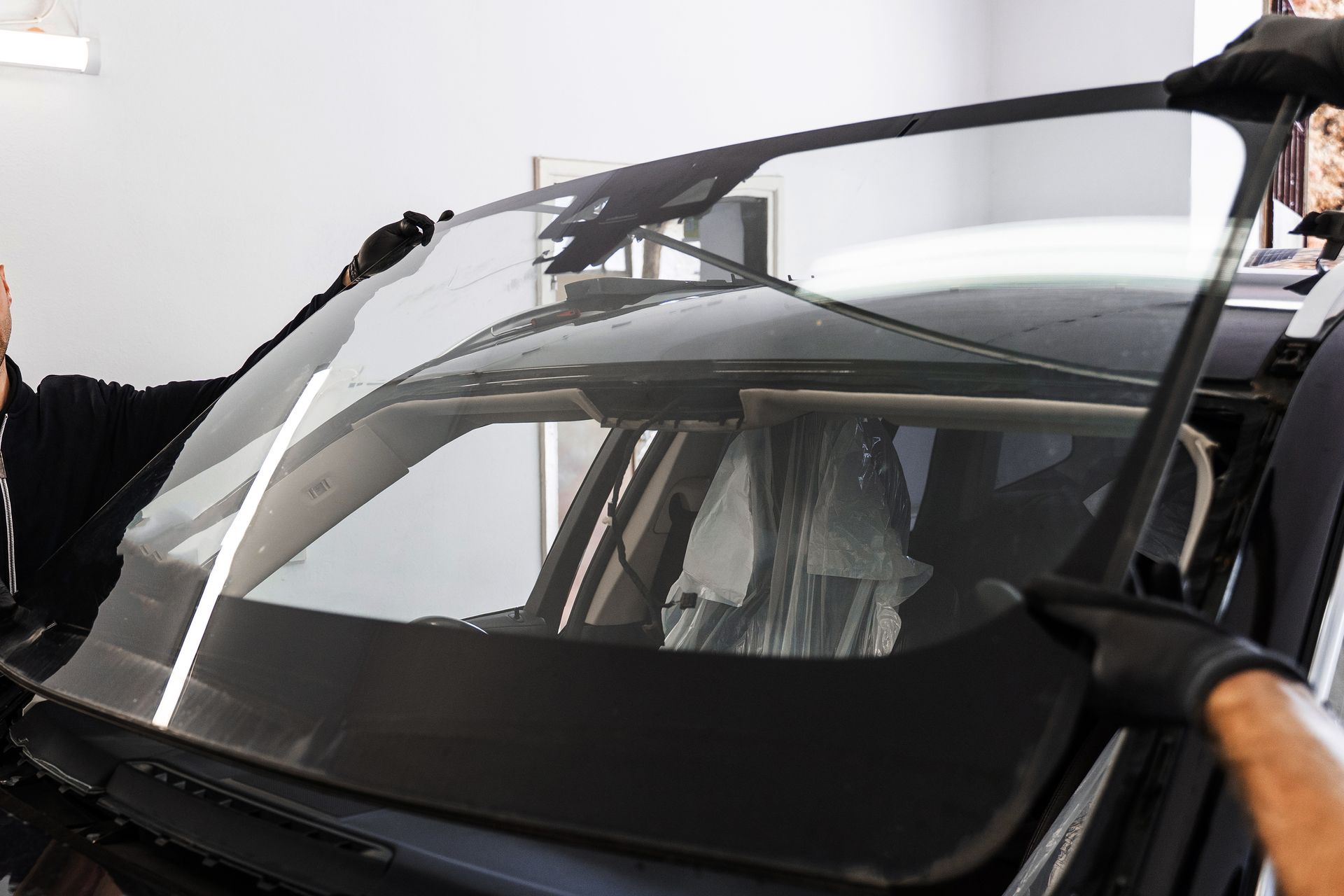 Person replacing a car windshield in a garage. Black car, clear glass, black gloves.