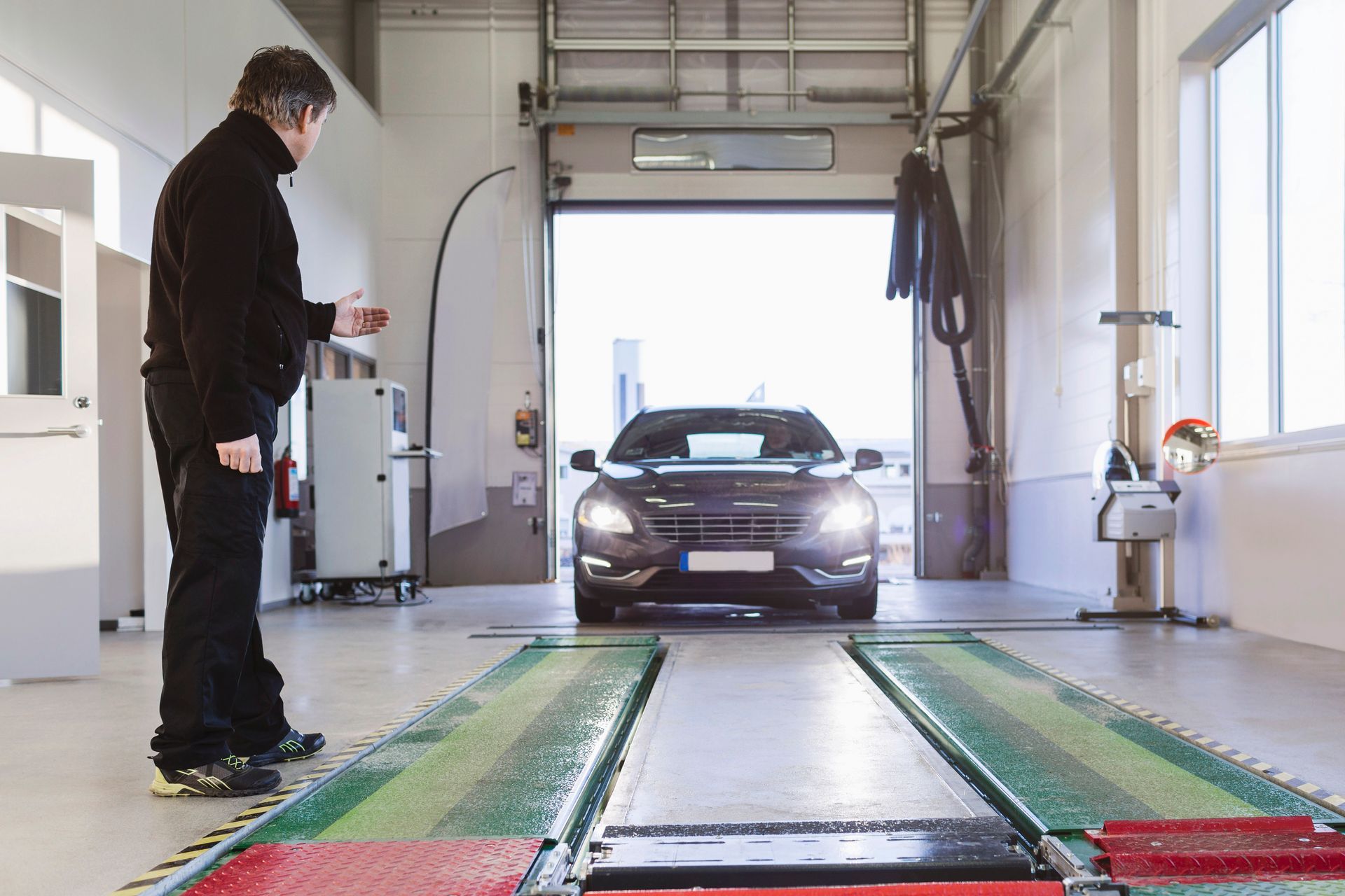 A mechanic guides a car onto a testing platform inside a repair shop.
