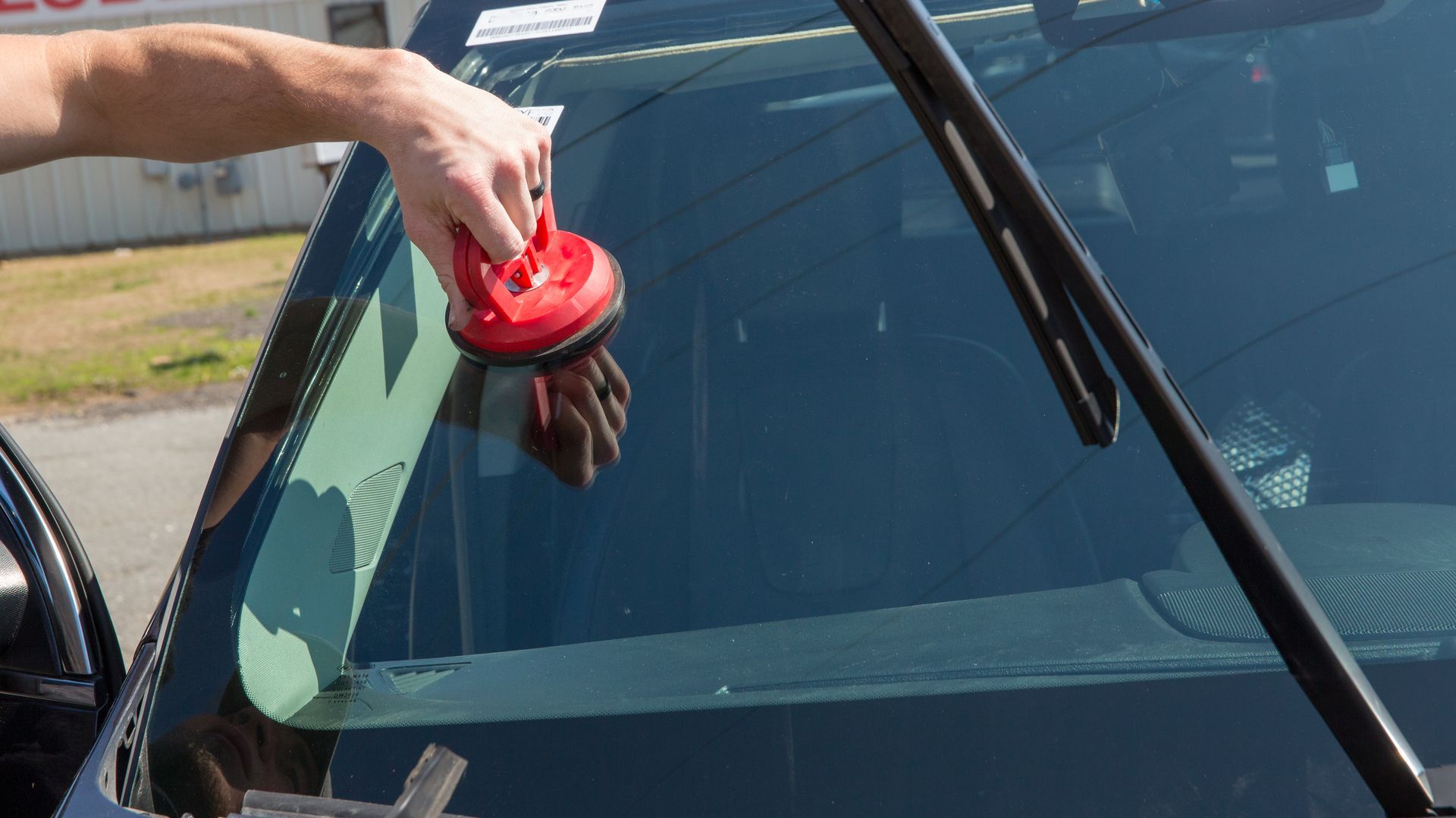 Person using a red suction cup tool to remove a windshield from a black car.