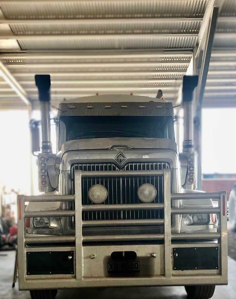 Silver semi-truck with bull bar, two headlights, and two exhaust stacks indoors.