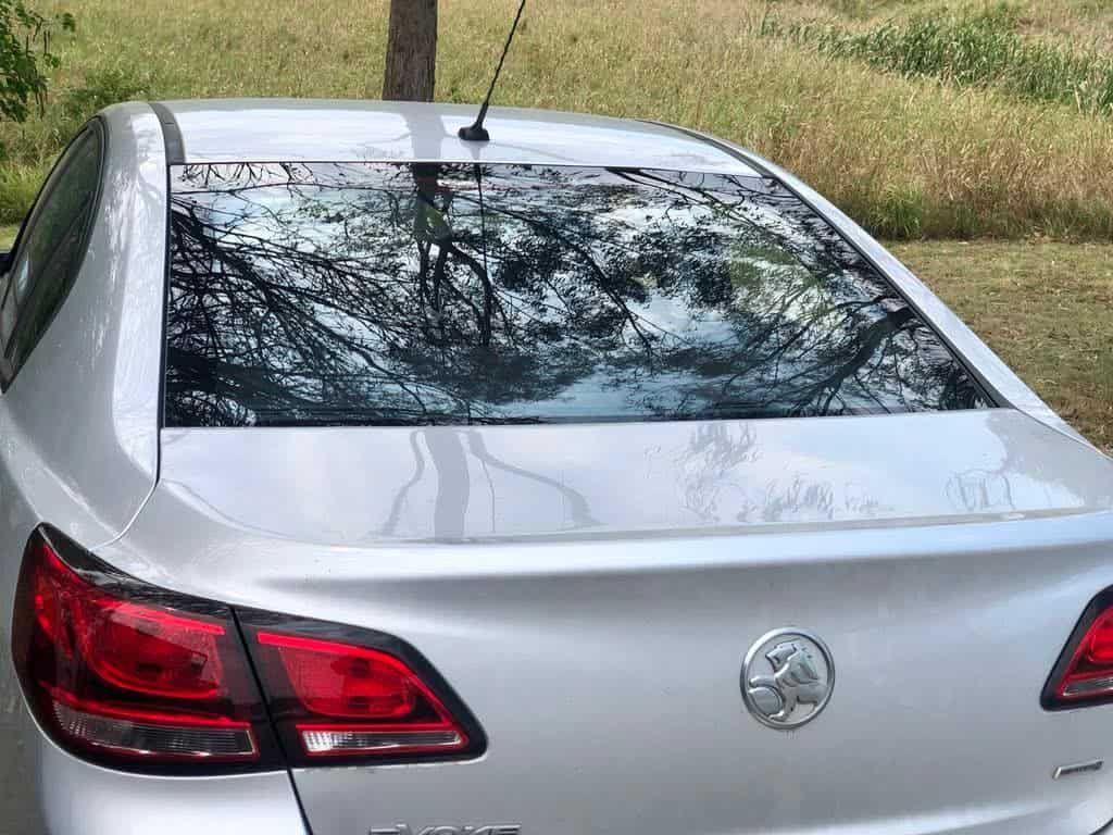 Silver sedan with reflective rear window showing tree canopy.