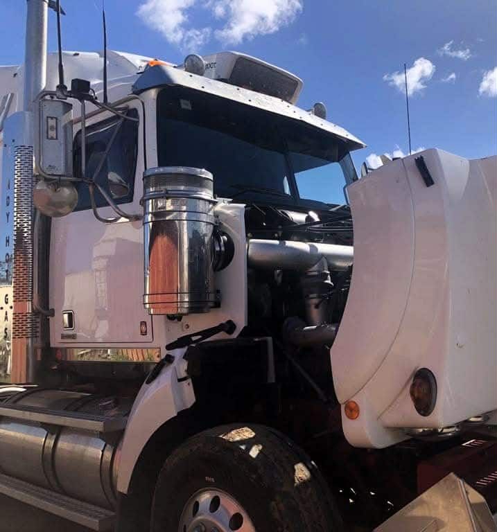 White semi-truck with open hood, parked on a sunny day.