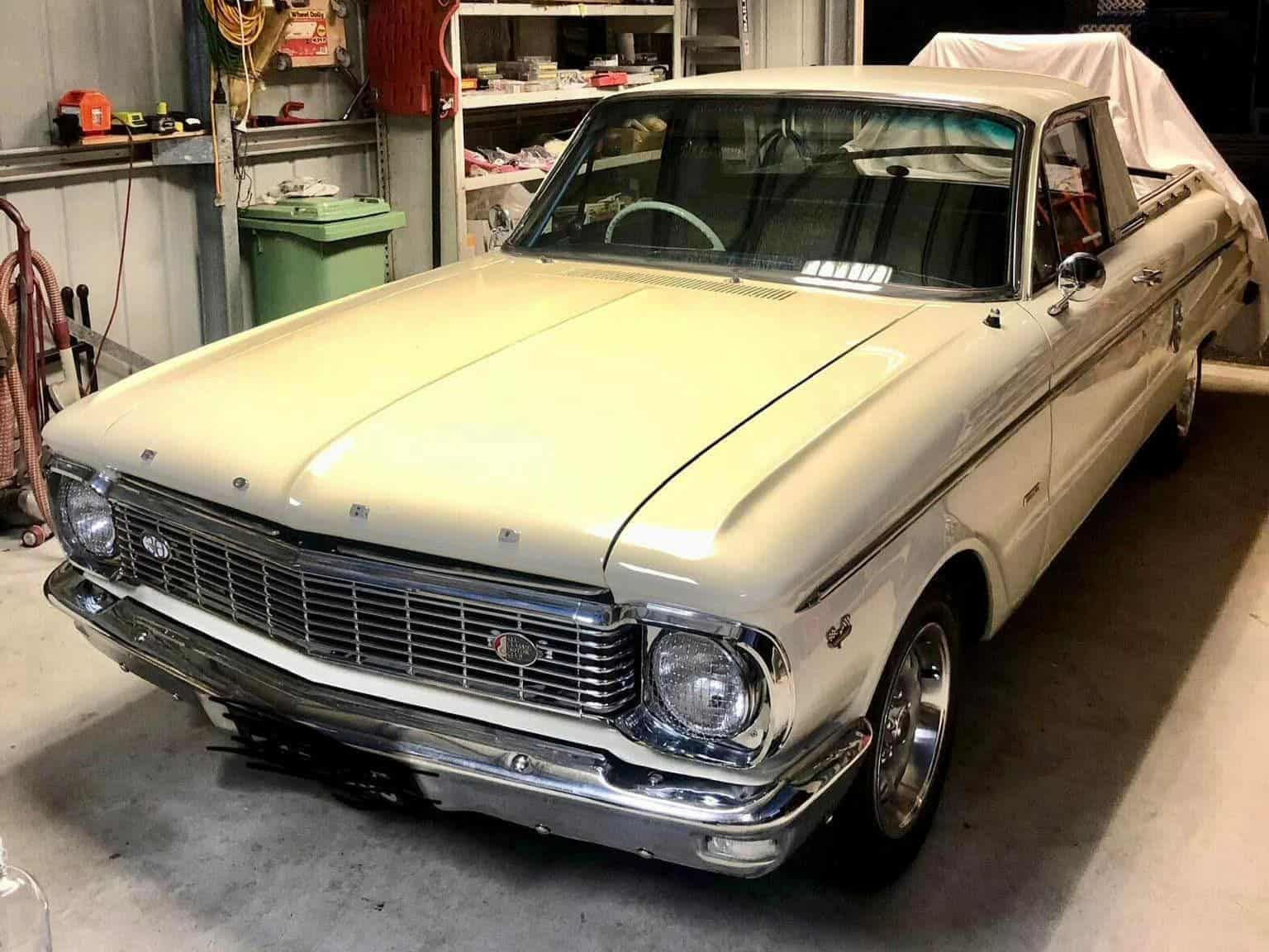 Cream-colored vintage Ford Falcon ute parked inside a garage. Chrome trim and a white steering wheel are visible.