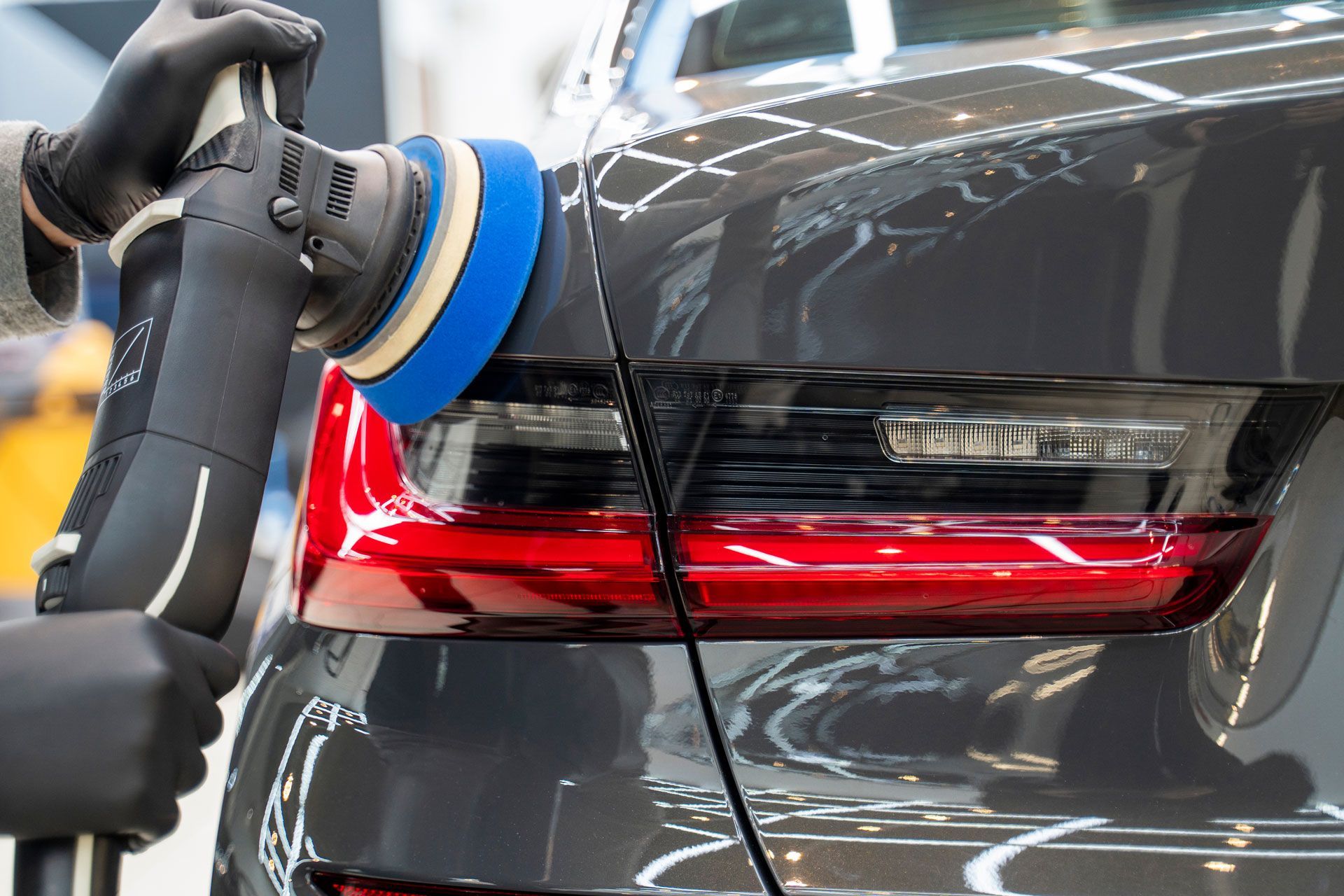 Person polishing a dark gray car with a power buffer.