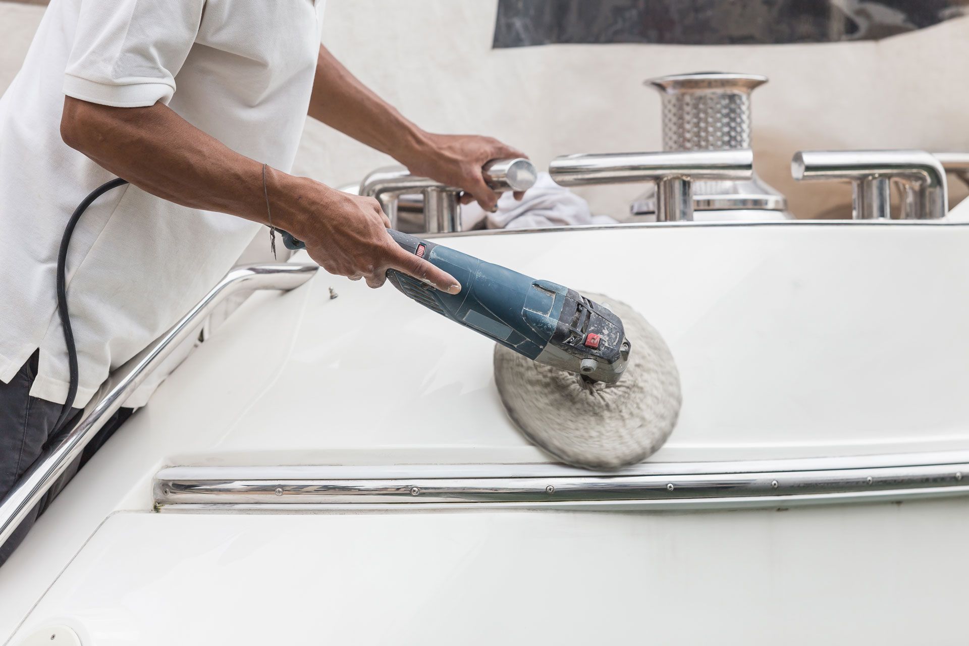Person polishing a white boat with a power buffer.