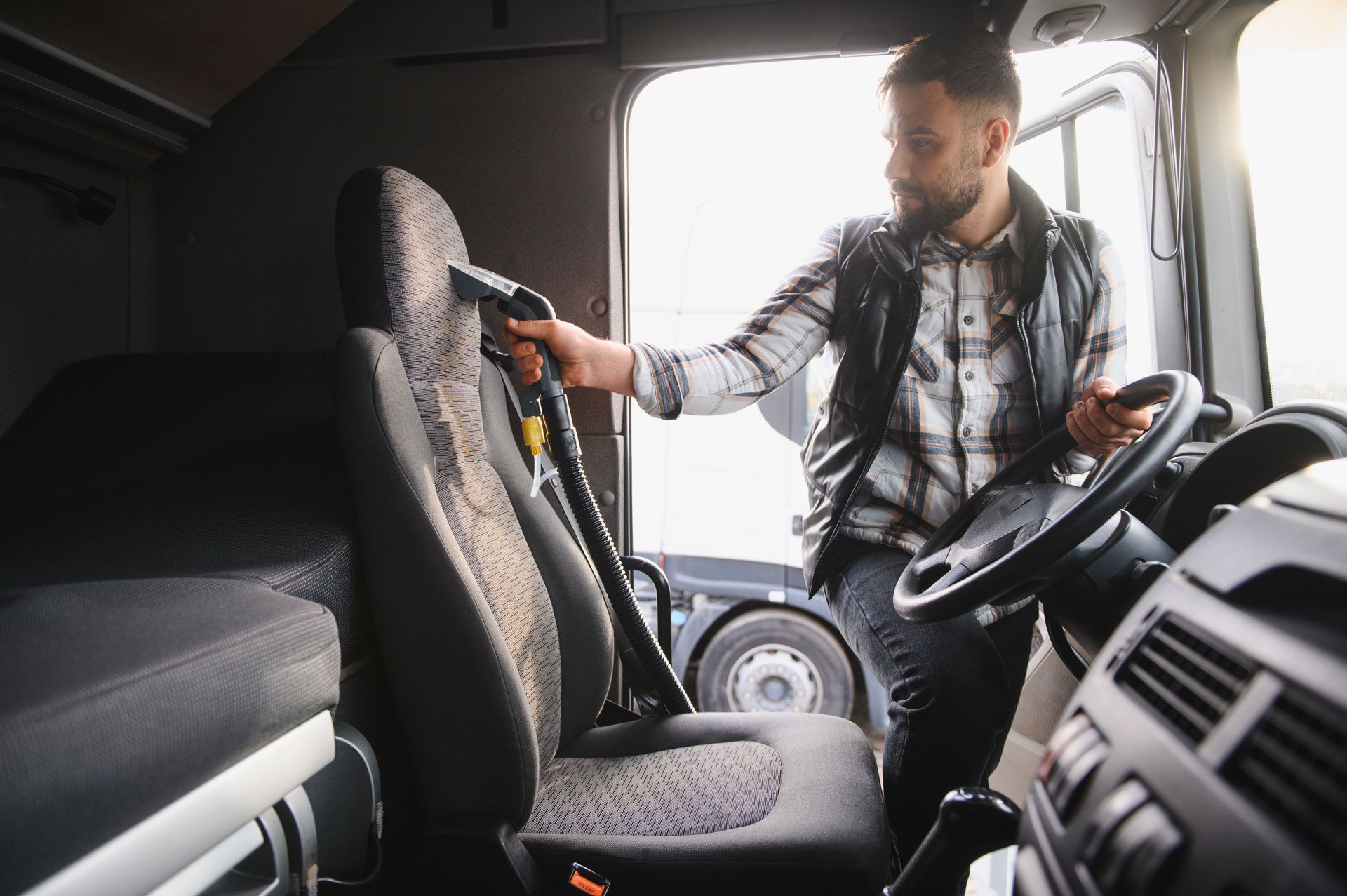 A person vacuuming the seat of a truck cabin; the person is holding the vacuum hose.
