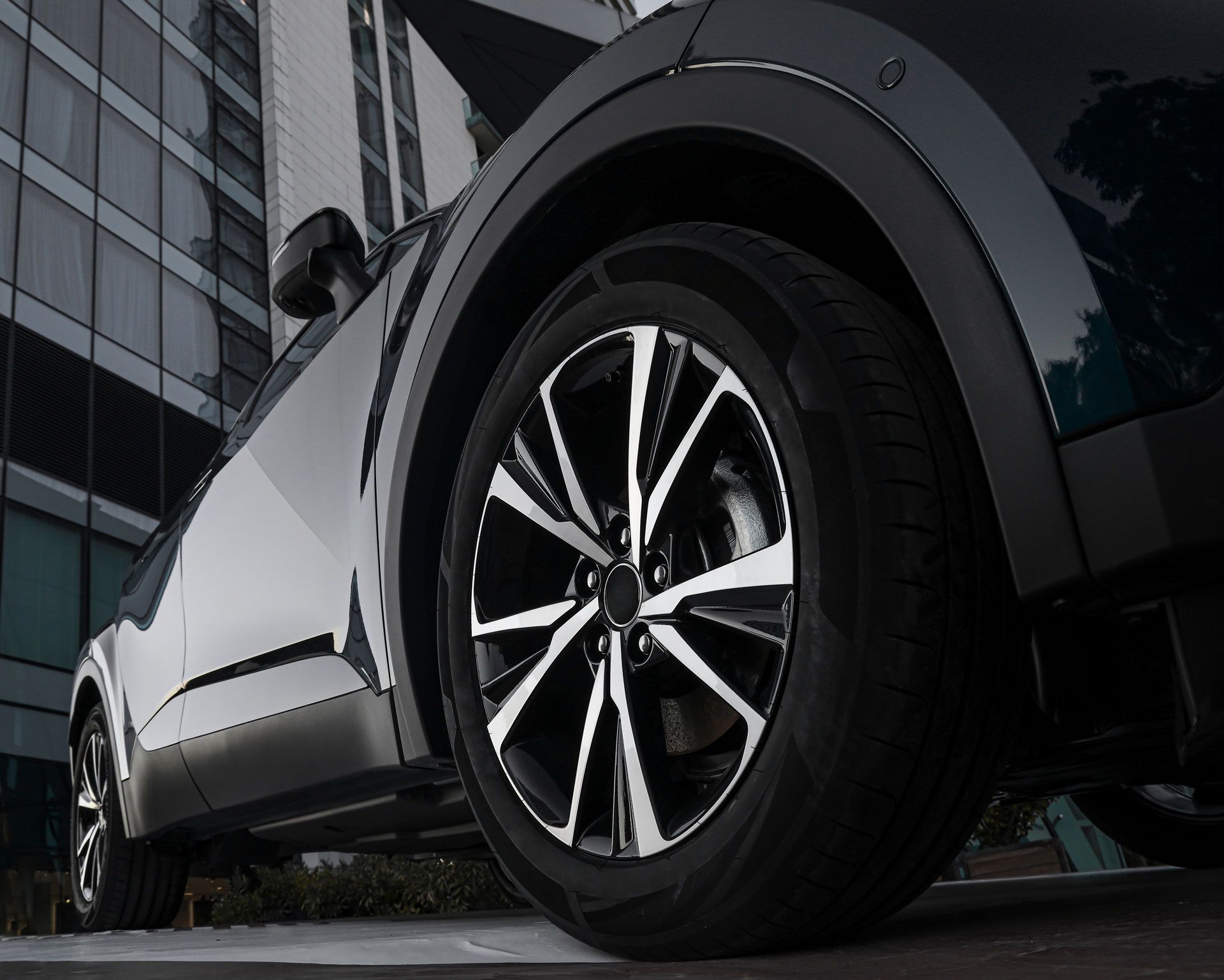 Black car tire and wheel, with reflective surface, against an urban backdrop.