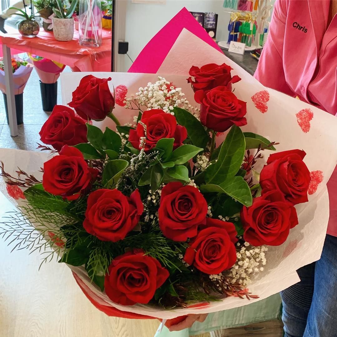 A Woman in A Pink Jacket Is Holding a Bouquet of Red Roses — Ivy Lane Flowers & Gifts in Caloundra, QLD