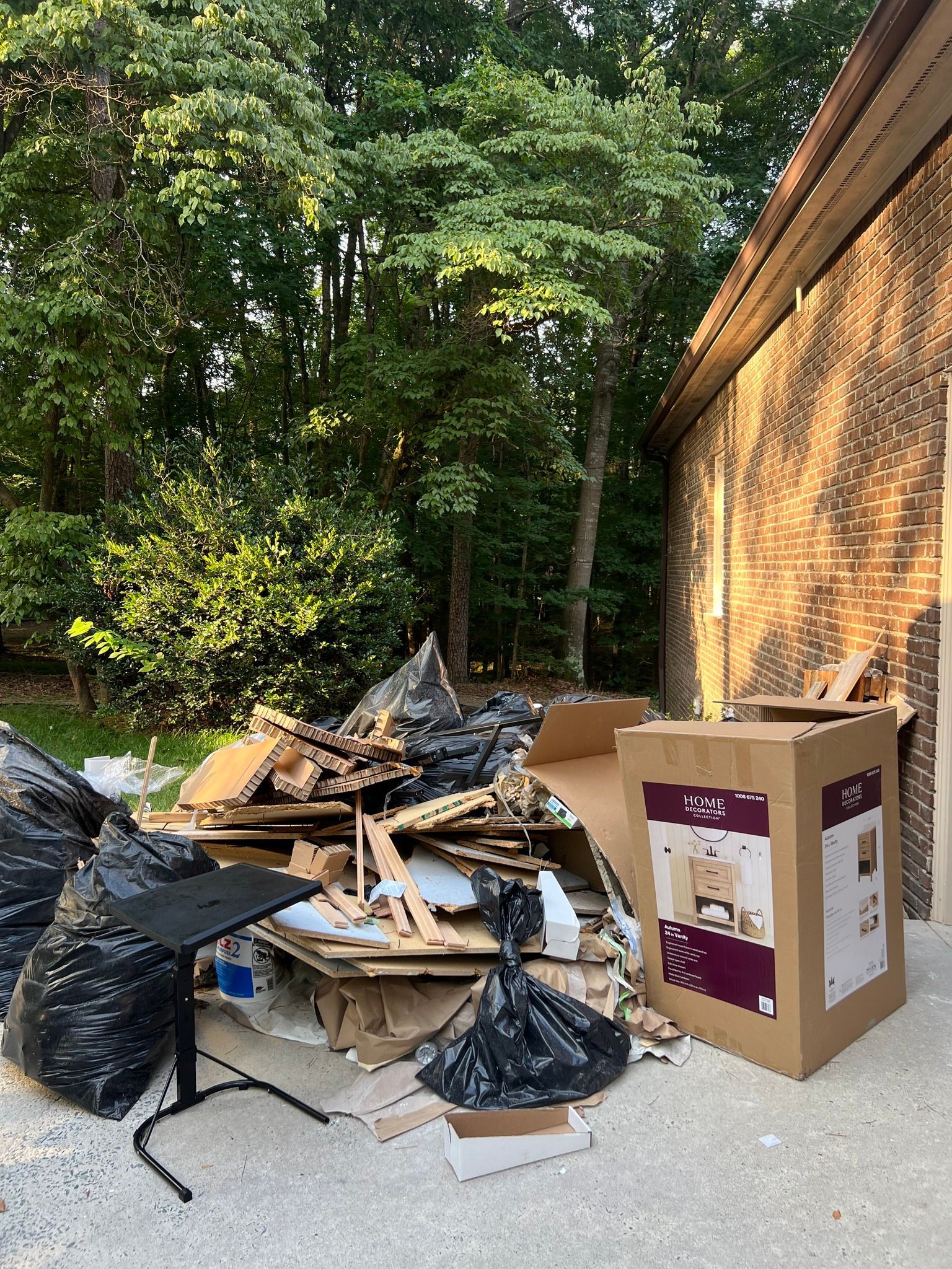 A pile of trash, cardboard boxes, and black plastic bags sitting on a gravel surface next to a brick building.