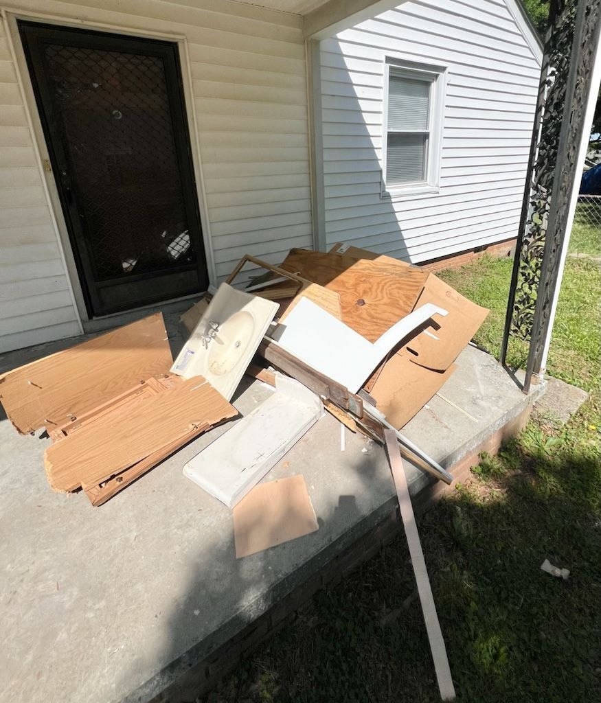 A stack of cardboard boxes and packing materials resting on a concrete porch in front of a white house.