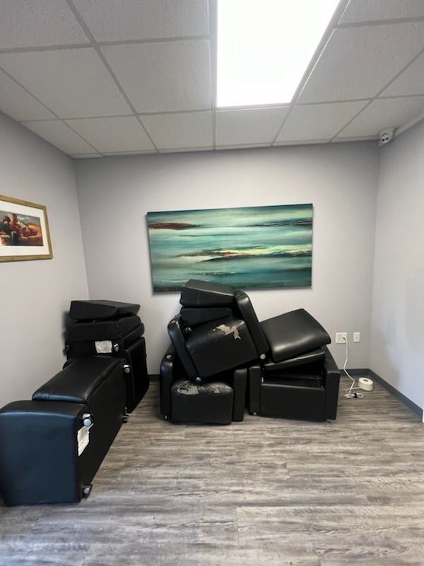 Several black upholstered chairs are stacked and clustered against a gray wall under a horizontal abstract painting.
