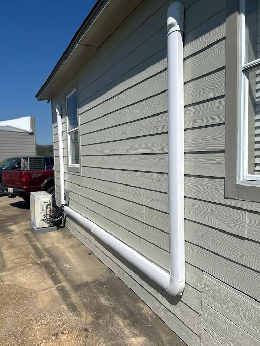 White PVC pipe runs vertically and horizontally along the side of a light gray building with windows.