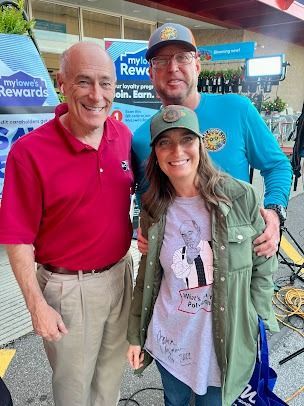 Three people smiling at a Lowe's store. One wears red shirt, khaki pants. Another wears a green jacket. The third has on a blue shirt.