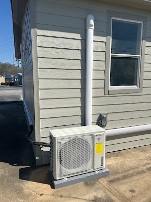 Air conditioning unit on a concrete base, mounted on a building exterior with vertical and horizontal pipes.
