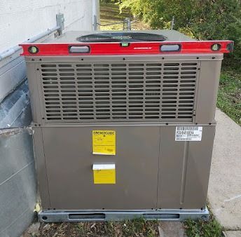 An air conditioning unit with a level on top, outdoors, near a building.