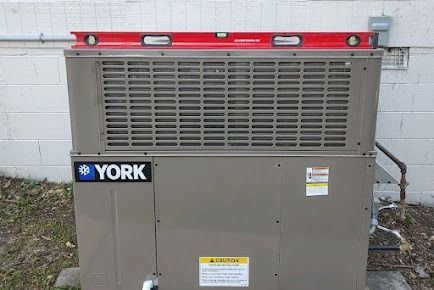 A red level rests on top of a York HVAC unit, testing levelness against a white wall.